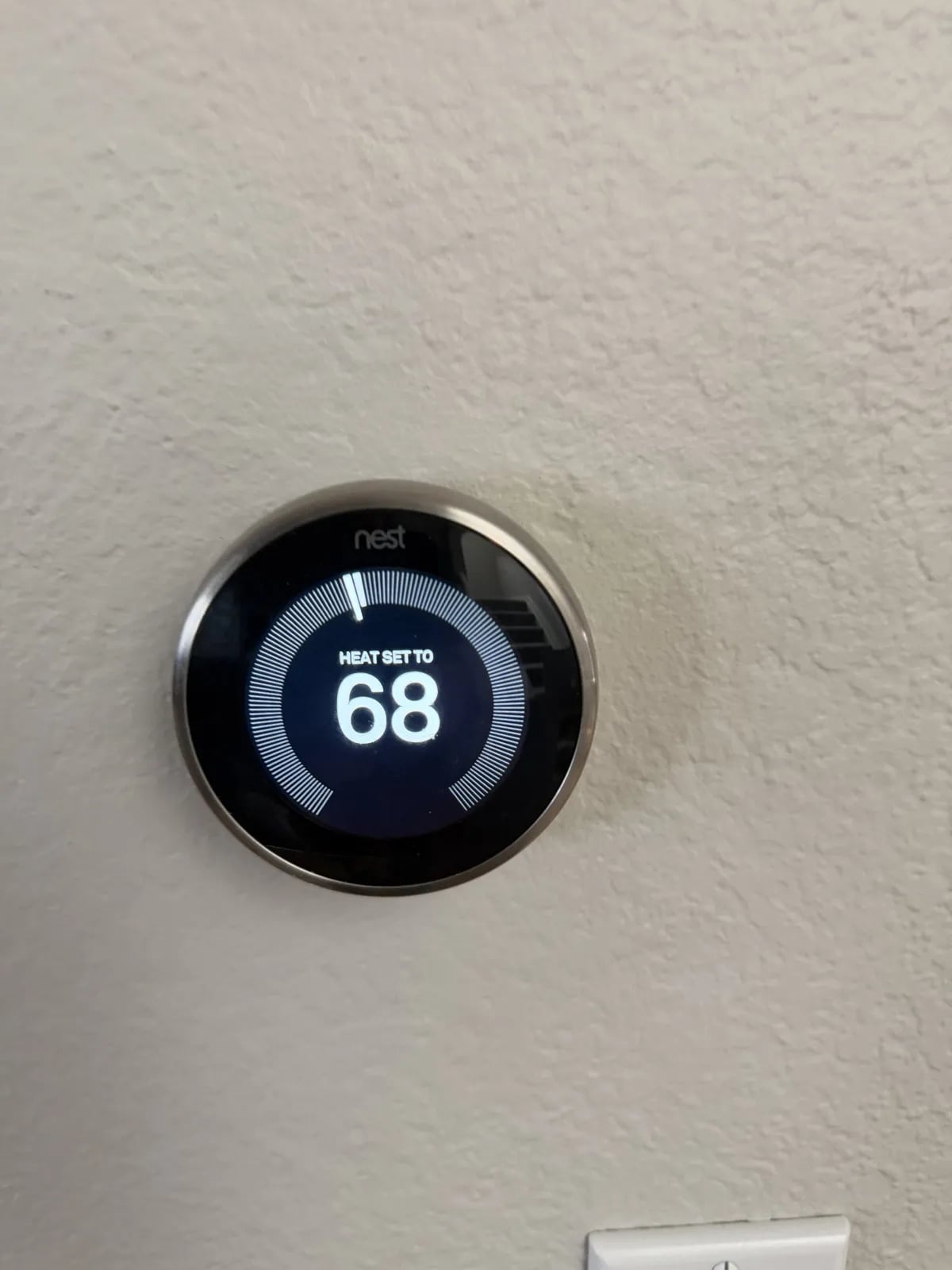 A Nest thermostat on a beige wall set to heat to 68 degrees